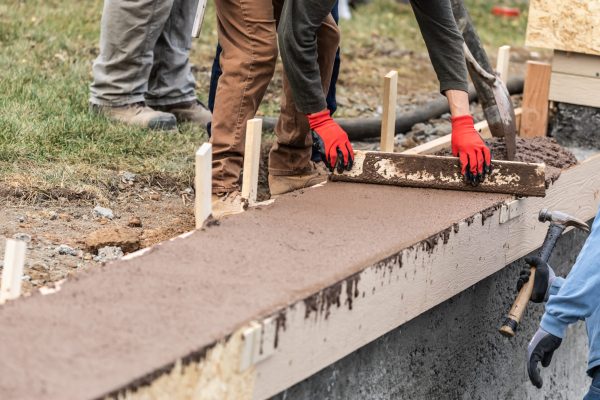 Construction Workers Pouring And Leveling Wet Cement Into Wood Framing.